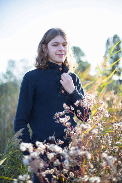 Smiling white young man with long hair with trees behind in field - Photo, image