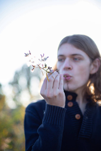 White european young man with long hair portrait focus is on the branch in his hand - Foto, Bild