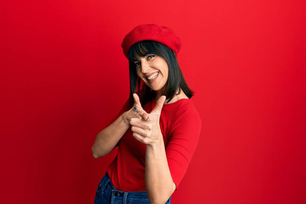 Young hispanic woman wearing french look with beret pointing fingers to camera with happy and funny face. good energy and vibes.  - Photo, Image
