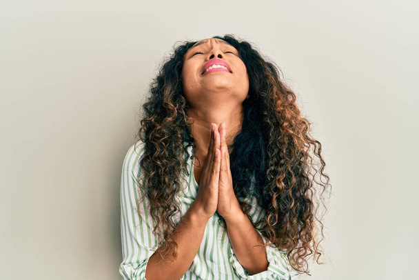 Jovem mulher latina vestindo roupas casuais implorando e orando com as mãos, juntamente com a expressão da esperança no rosto muito emocional e preocupado. implorando.  - Foto, Imagem
