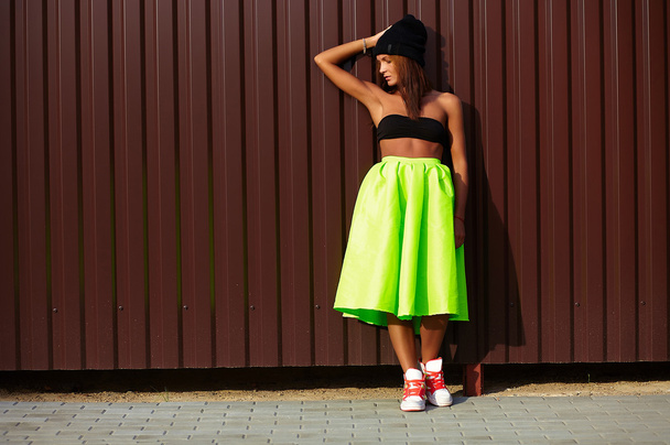 Portrait of sexy teenager urban modern young stylish woman girl  model in bright modern cloth in green colotful skirt outdoors in the street standing near wall - Foto, imagen