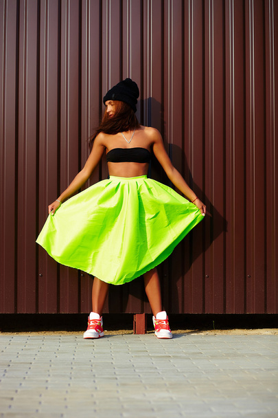 Portrait of sexy teenager urban modern young stylish woman girl  model in bright modern cloth in green colotful skirt outdoors in the street standing near wall - Foto, imagen