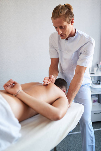 Therapist doing back massage on professional table in salon, spa relaxation - Foto, afbeelding