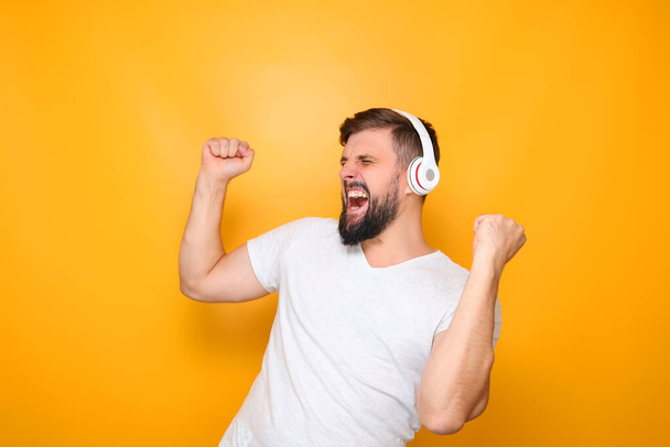 een man met een witte koptelefoon luistert naar muziek en zingt luid, steekt zijn handen op. - Foto, afbeelding