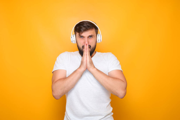 muž poslouchající hudbu s bílými sluchátky založenými dlaněmi před obličejem. - Fotografie, Obrázek
