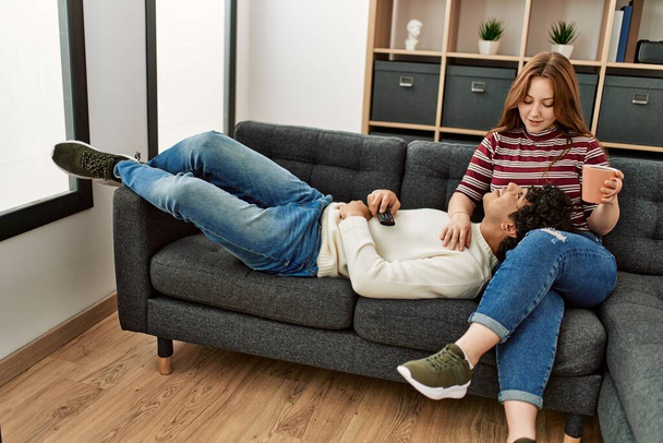 Jovem casal sorrindo feliz beber xícara de café sentado no sofá em casa. - Foto, Imagem