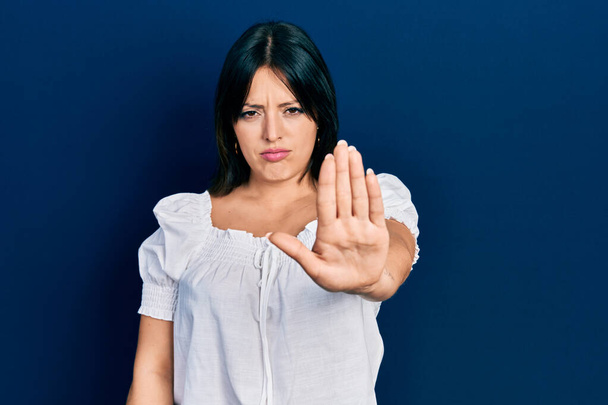 Mujer hispana joven usando ropa casual haciendo dejar de cantar con la palma de la mano. expresión de advertencia con gesto negativo y grave en la cara.  - Foto, imagen