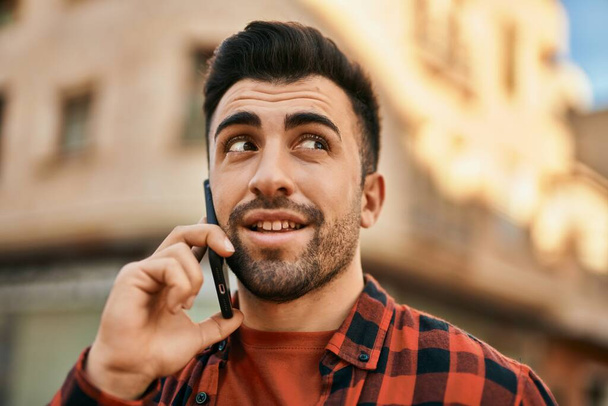 Genç İspanyol adam gülümsüyor. Şehirdeki akıllı telefondan konuşuyor.. - Fotoğraf, Görsel