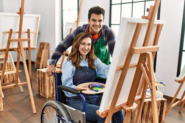 Opettaja ja vammainen maali opiskelija istuu pyörätuolilla hymyillen onnellinen maalaus taidekoulussa. - Valokuva, kuva