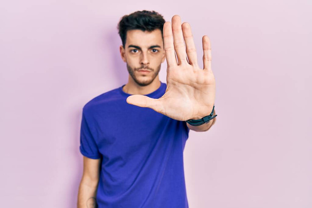 Young hispanic man wearing casual t shirt doing stop sing with palm of the hand. warning expression with negative and serious gesture on the face.  - Photo, Image