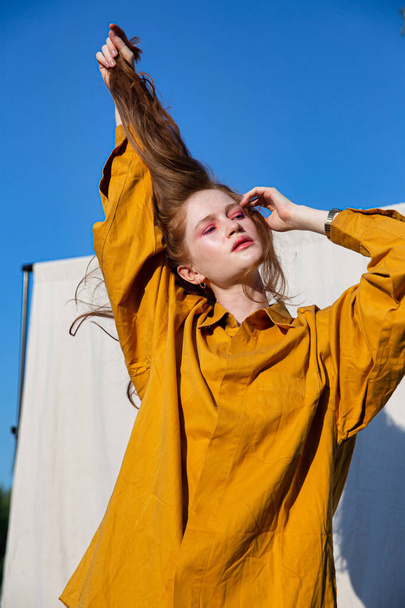 White european girl with dark hair in yellow clothes with closed eyes and blue sky behind - 写真・画像