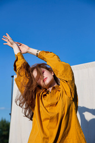 European white girl with dark hair in yellow clothes with closed eyes and blue sky behind - Foto, afbeelding