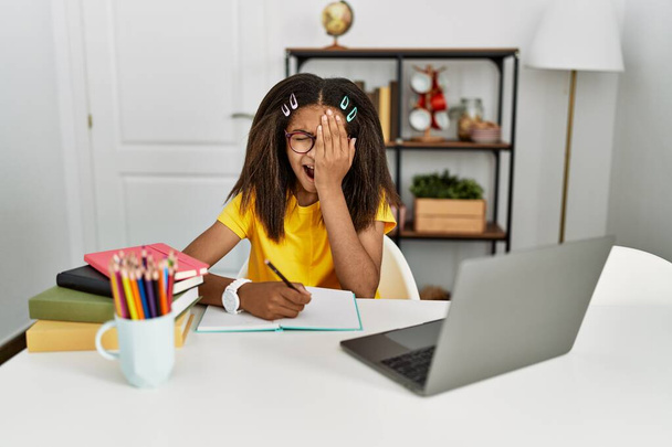 Young african american girl doing homework at home yawning tired covering half face, eye and mouth with hand. face hurts in pain.  - Foto, imagen