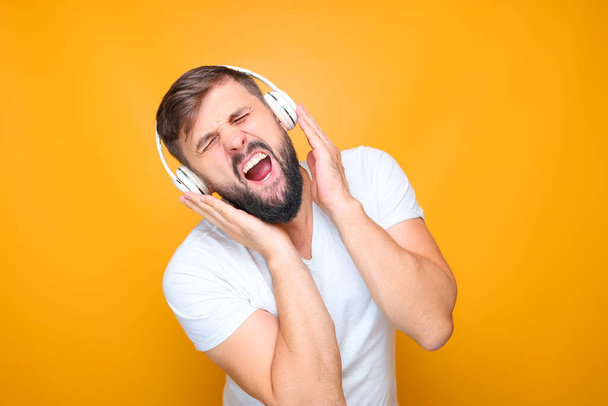 szakállas férfi fehér zenei fejhallgatóval egyszerre hallgat zenét és énekel. - Fotó, kép