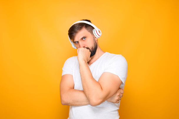 un hombre con auriculares blancos escucha música y reflexiona, poniendo su mano en su cara. - Foto, imagen