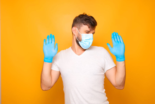 ένας άνδρας με ιατρική μάσκα και αποστειρωμένα γάντια μιας χρήσης δείχνει διάφορες χειρονομίες. - Φωτογραφία, εικόνα