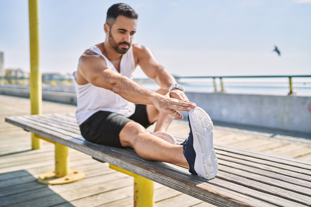 Hispanic man stretching legs after working out outdoors on a sunny day - Photo, Image