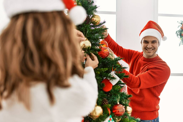 Jeune couple hispanique décorer arbre de Noël à la maison. - Photo, image