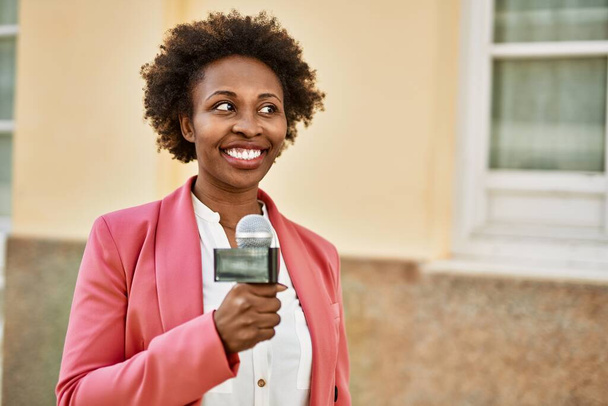 Молодая американская журналистка из Африки держит в руках микрофон репортера и улыбается в камеру для телевизионных новостей - Фото, изображение