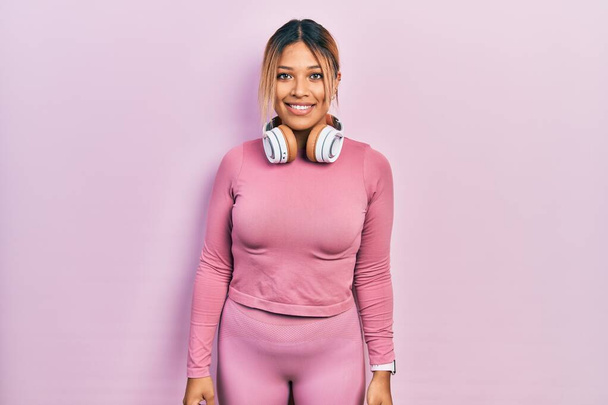 Beautiful hispanic woman wearing gym clothes and using headphones with a happy and cool smile on face. lucky person.  - Photo, Image
