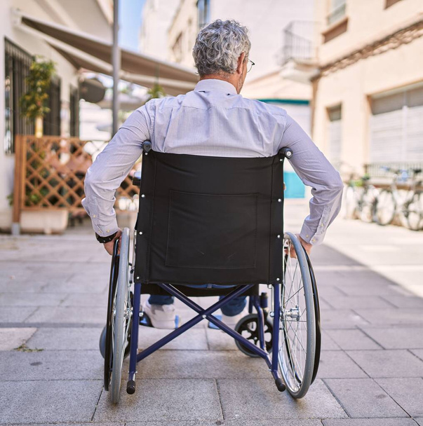 Moyen Age homme hispanique portant des vêtements de travail assis sur fauteuil roulant dans la rue - Photo, image