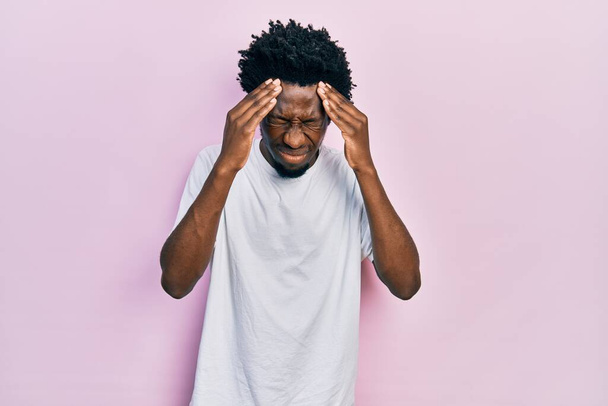 Junger afrikanisch-amerikanischer Mann in lässigem weißem T-Shirt mit der Hand auf dem Kopf wegen Kopfschmerzen wegen Stress. Migräne.  - Foto, Bild