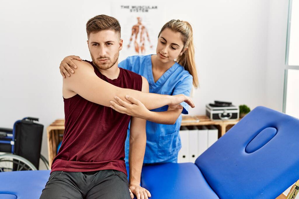 Young hispanic physioterapist woman make arm rehab treatment to man at the clinic. - 写真・画像