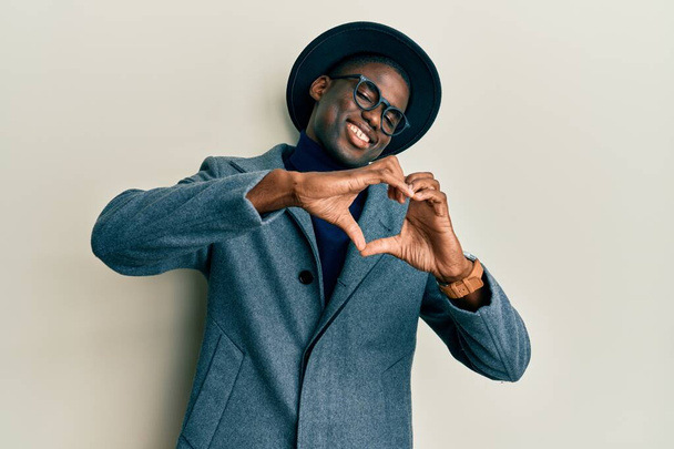 Jonge Afro-Amerikaanse man draagt elegante stijl glimlachend in liefde doen hart symbool vorm met handen. romantisch concept.  - Foto, afbeelding