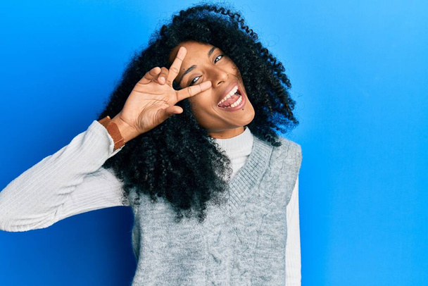 Afrikai amerikai nő afro haj visel alkalmi téli pulóver csinál béke szimbólum ujjaival az arcon, mosolygós vidám bemutató győzelem  - Fotó, kép