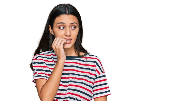 Menina hispânica jovem vestindo roupas casuais olhando estressado e nervoso com as mãos na boca mordendo unhas. problema de ansiedade.  - Foto, Imagem