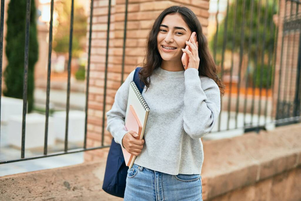 Joven estudiante de Oriente Medio sonriendo feliz hablando en el teléfono inteligente en la ciudad. - Foto, imagen
