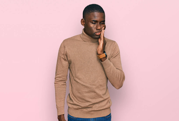 Fiatal afro-amerikai férfi alkalmi téli pulóvert visel, kéz a kézben, fájdalmas kifejezéssel, fogfájás vagy fogbetegség miatt. fogorvos  - Fotó, kép