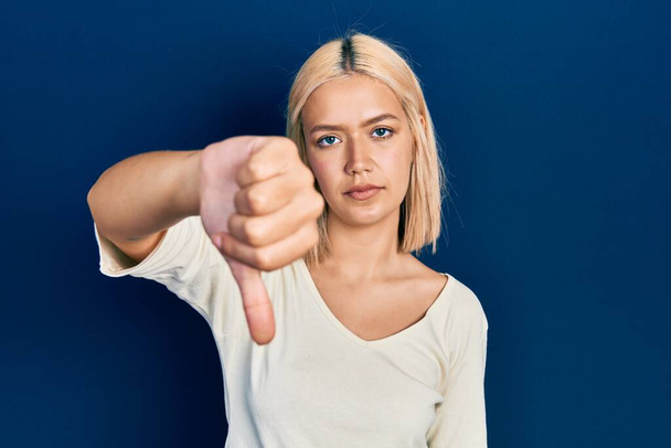 Beautiful blonde woman wearing casual sweater looking unhappy and angry showing rejection and negative with thumbs down gesture. bad expression.  - Photo, Image