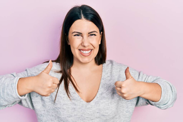 Молодая испаноязычная женщина в повседневной одежде знак успеха делает позитивный жест с рукой, большие пальцы вверх улыбается и счастлив. веселое выражение лица и жест победителя.  - Фото, изображение