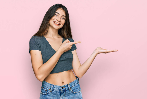 Young beautiful teen girl wearing casual crop top t shirt amazed and smiling to the camera while presenting with hand and pointing with finger.  - Fotografie, Obrázek