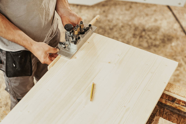 Carpenter working on a wooden panel or sheet in a woodworking or joinery workshop in a high angle cropped view of his hands and equipment with copyspace - Foto, Imagem
