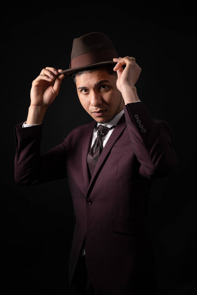 A Caucasian man from Spain in suit on black background with hands on hat - Foto, imagen