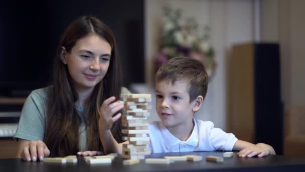 Мать и сын играют в настольную игру с деревянной башней дома - Кадры, видео
