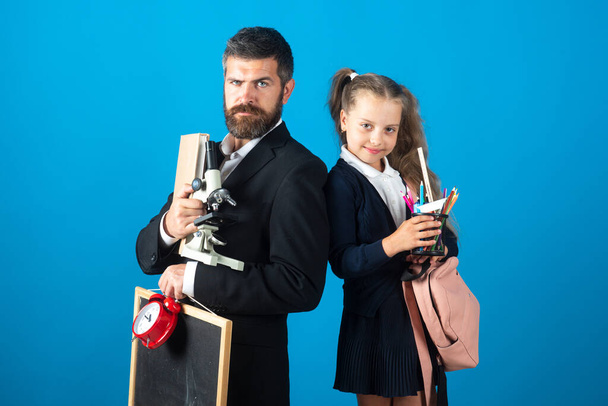 Father and pupil daughter ready to school. Portrait of dad and little girls with school supplies, isolated on blue background. - Foto, Bild