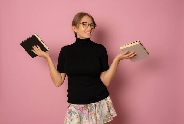 Photo of young beautiful smiling positive cheerful girl in glasses with books isolated on pink color background - Фото, изображение