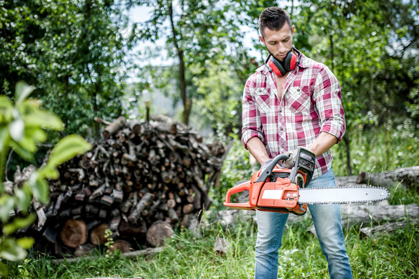 Portrait of aggressive, muscular and athletic man with chainsaw getting ready for fire wood cutting - Foto, Imagem