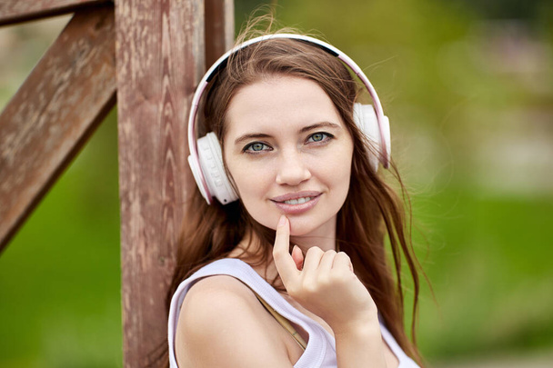 Portrait of young caucasian woman in wireless headphones in park. - Photo, image