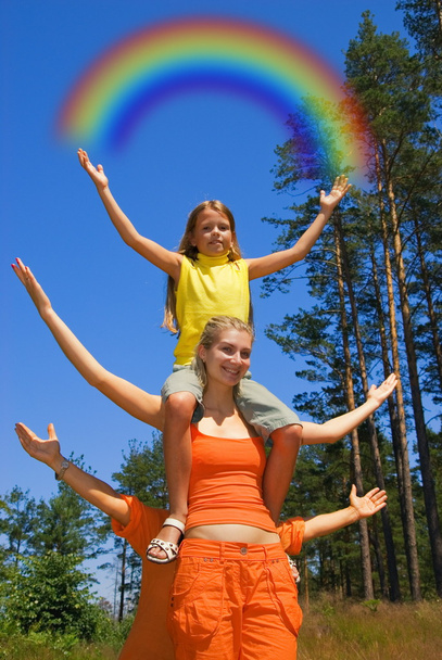 Small girl sitting on a sister's shoulders holding rainbow in - Photo, Image