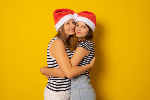 Glückliche Mutter und Tochter zusammen im Weihnachtsmann-Hut über gelbem Hintergrund. Weihnachtskonzept. - Foto, Bild