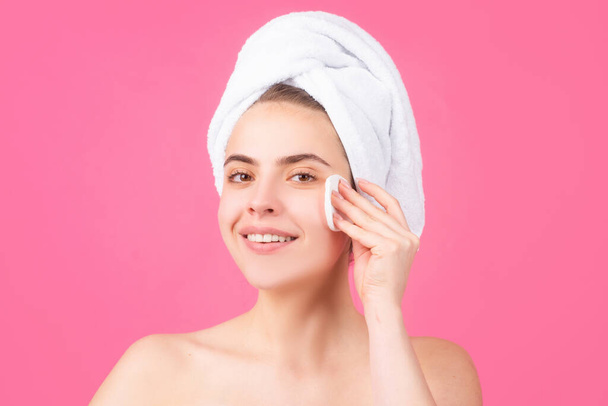 Beautiful girl with a towel on head clean remove cosmetics from face use cotton patch isolated over pink background. Facial treatment, cosmetology, beauty and spa. - Foto, immagini