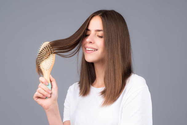 Brushing Hair. Portrait young smiling woman brushing straight natural hair with comb. Girl combing hair with hairbrush. Hair care beauty concept. - Foto, immagini