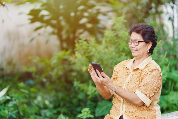 Una donna thailandese anziana sta usando uno smartphone per fare shopping o messaggiare con un viso sorridente. - Foto, immagini