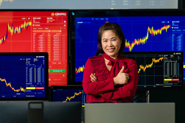 Ázsiai nő sikeres szakmai bróker kereskedő befektető stand mosoly keresztbe kar megjelenítése hüvelykujj fel nézd meg a kamera előtt számítógép képernyőjén állomány és bitcoin cryptocurrency grafikon elemzés. - Fotó, kép