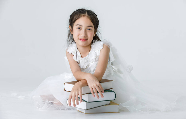 Muotokuva lähikuva eristetty studio laukaus Aasian kaunis tyttö pukeutuu valkoinen prinsessa pitkä ruusu kukka mekko muoti puku poseeraa pino kirjoja katso kameraa. - Valokuva, kuva