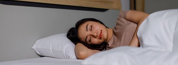Ritratto in alto ritratto di una giovane adorabile donna asiatica adulta che dorme sul suo fianco in una camera da letto di notte. Signora sdraiata su cuscino bianco e coperta con luce e ombra. Concetto di vita sana - Foto, immagini